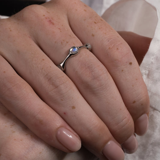 Close-up of a hand wearing a silver ring with moonstones on a neutral background